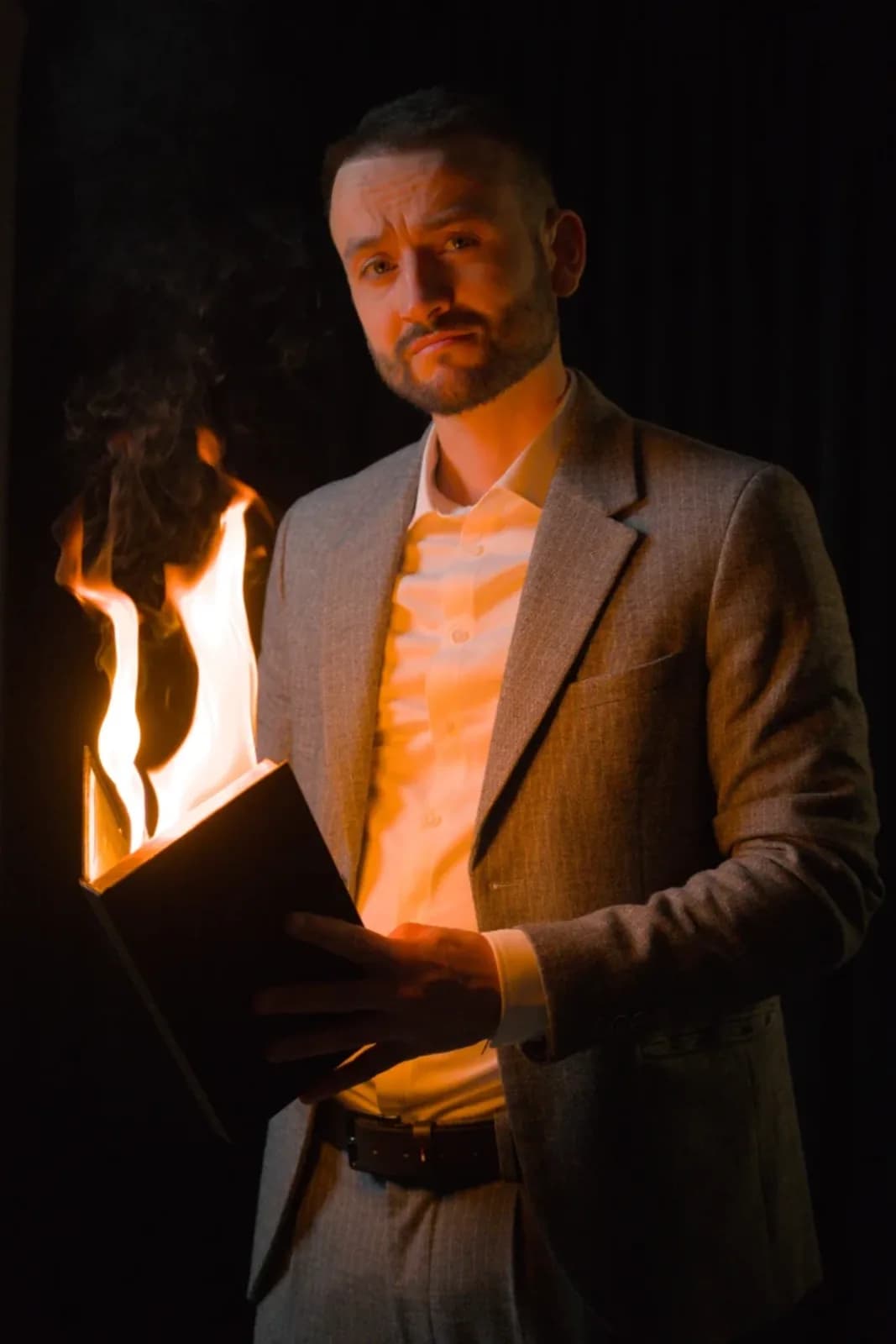 Tyson Dumas, magicien mentaliste, tenant un livre enflammé en costume gris — portrait studio